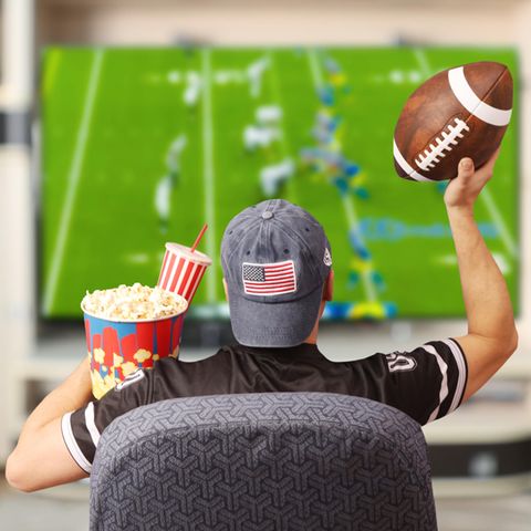 Super Bowl Gadgets: Footballfan sitzt mit Ball und Popcorn vor einem Fernseher
