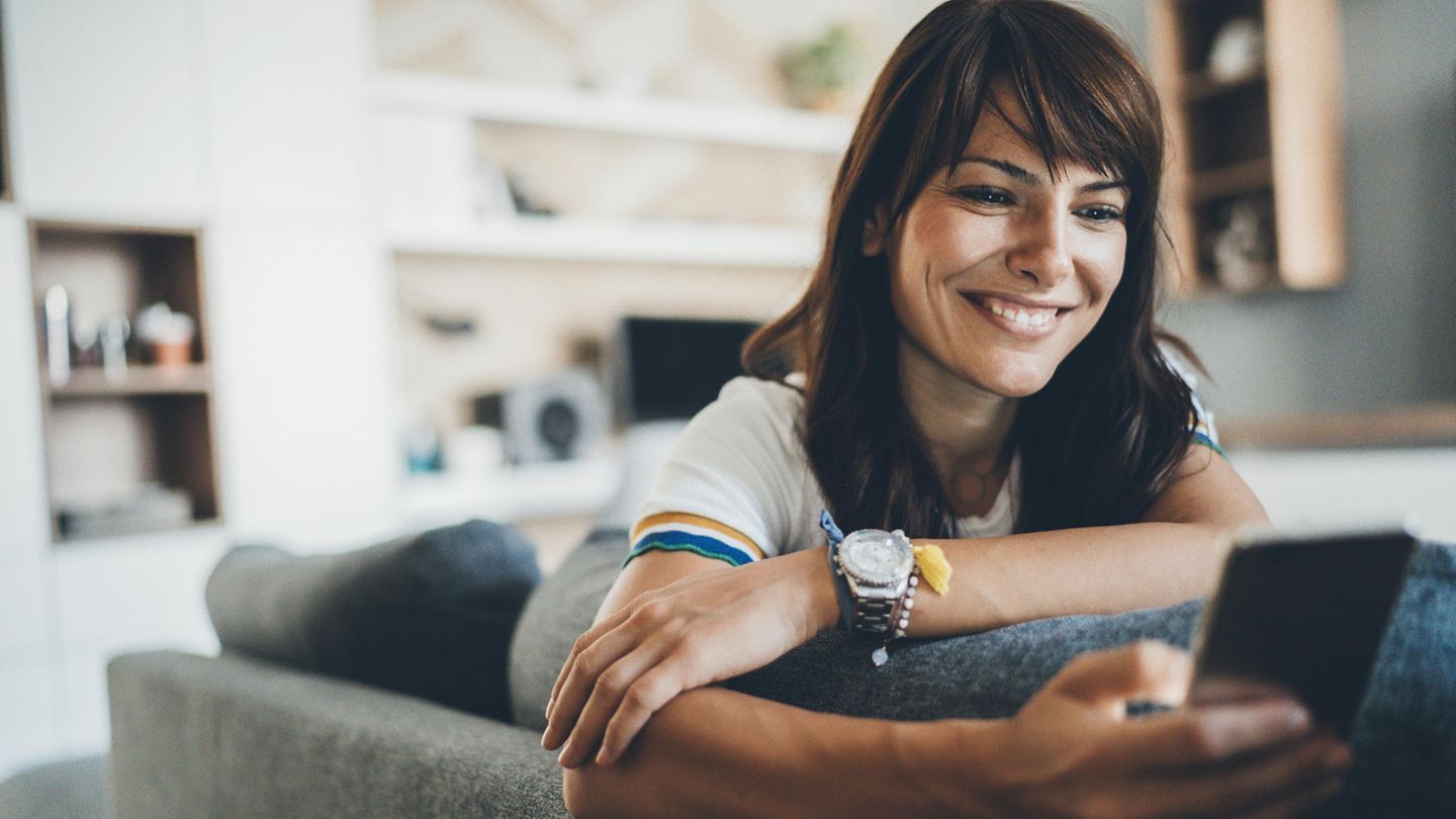 Frau sitzt mit Smartphone – möglicherweise Samsung Galaxy S24 – auf Sofa.