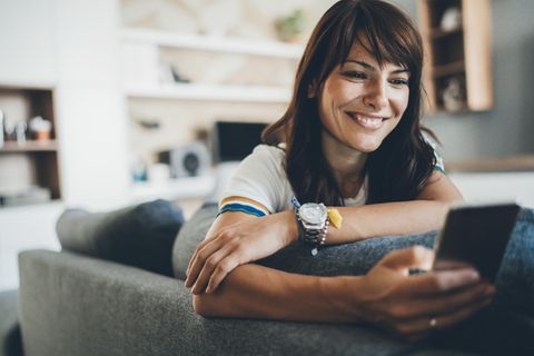 Frau sitzt mit Smartphone – möglicherweise Samsung Galaxy S24 – auf Sofa.