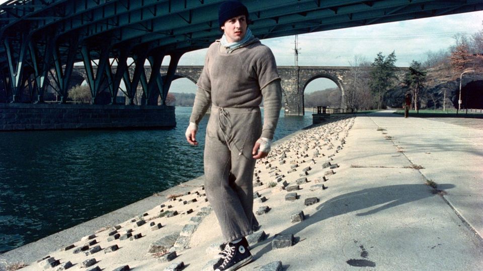 Sylvester Stallone as "Rocky" in gray jersey by a canal