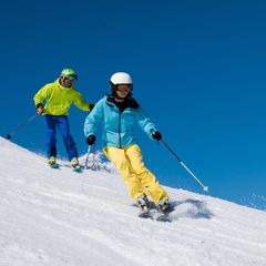 Geschenkideen für Skifahrer: Familie bei einer Abfahrt und strahlend blauem Himmer
