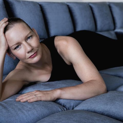 Porträt von Sandra Hüller, in schwarzem Kleid, liegend auf einem blauen Sofa