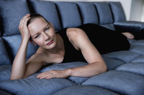 Porträt von Sandra Hüller, in schwarzem Kleid, liegend auf einem blauen Sofa