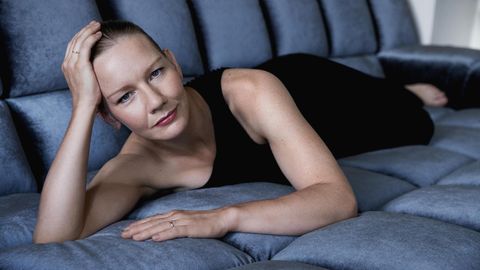 Porträt von Sandra Hüller, in schwarzem Kleid, liegend auf einem blauen Sofa