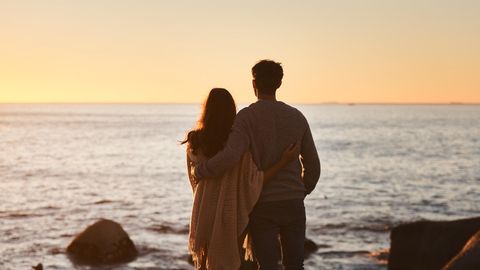 Ein Paar steht am Ufer des Meeres und blickt in den Sonnenuntergang.