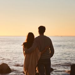 Ein Paar steht am Ufer des Meeres und blickt in den Sonnenuntergang.