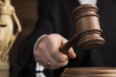 Eine Richterin mit einem Gerichtshammer im Hintergrund die Figur einer Justicia