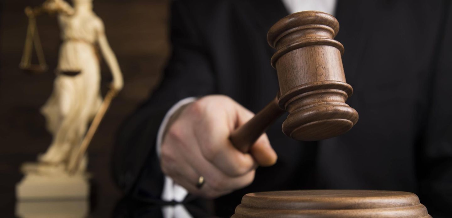 Eine Richterin mit einem Gerichtshammer im Hintergrund die Figur einer Justicia