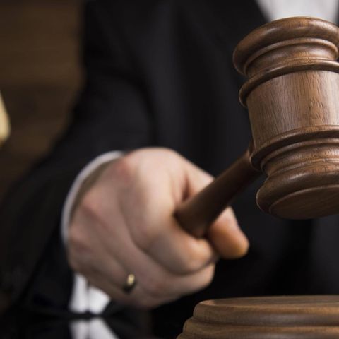 Eine Richterin mit einem Gerichtshammer im Hintergrund die Figur einer Justicia