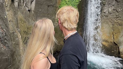 Ein junges Paar steht vor einem Wasserfall und schaut in die Tiefe