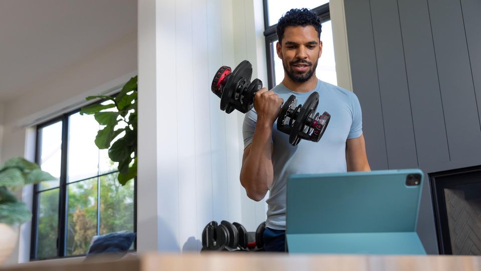 Sportlicher Mann trainiert mit den 552i Dumbbells von BowFlex im Wonzimmer