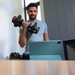Sportlicher Mann trainiert mit den 552i Dumbbells von BowFlex im Wonzimmer