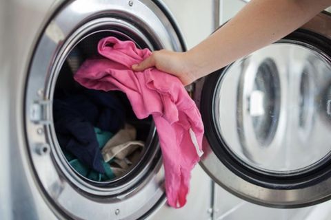Eine Person legt ein pinkes Kleidungsstück in eine Waschmaschine