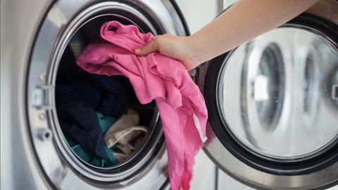 Eine Person legt ein pinkes Kleidungsstück in eine Waschmaschine