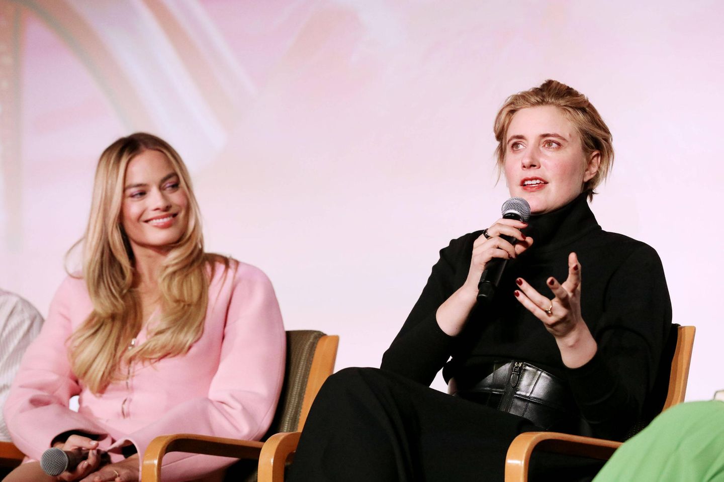 Greta Gerwig und Margot Robbie während der Fragerunde vor einem rosa Hintergrund