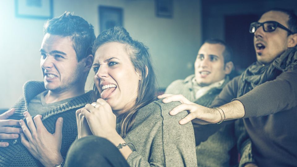 Gruppe junger Menschen zeigen vor dem Fernseher angeekelte Gesichter