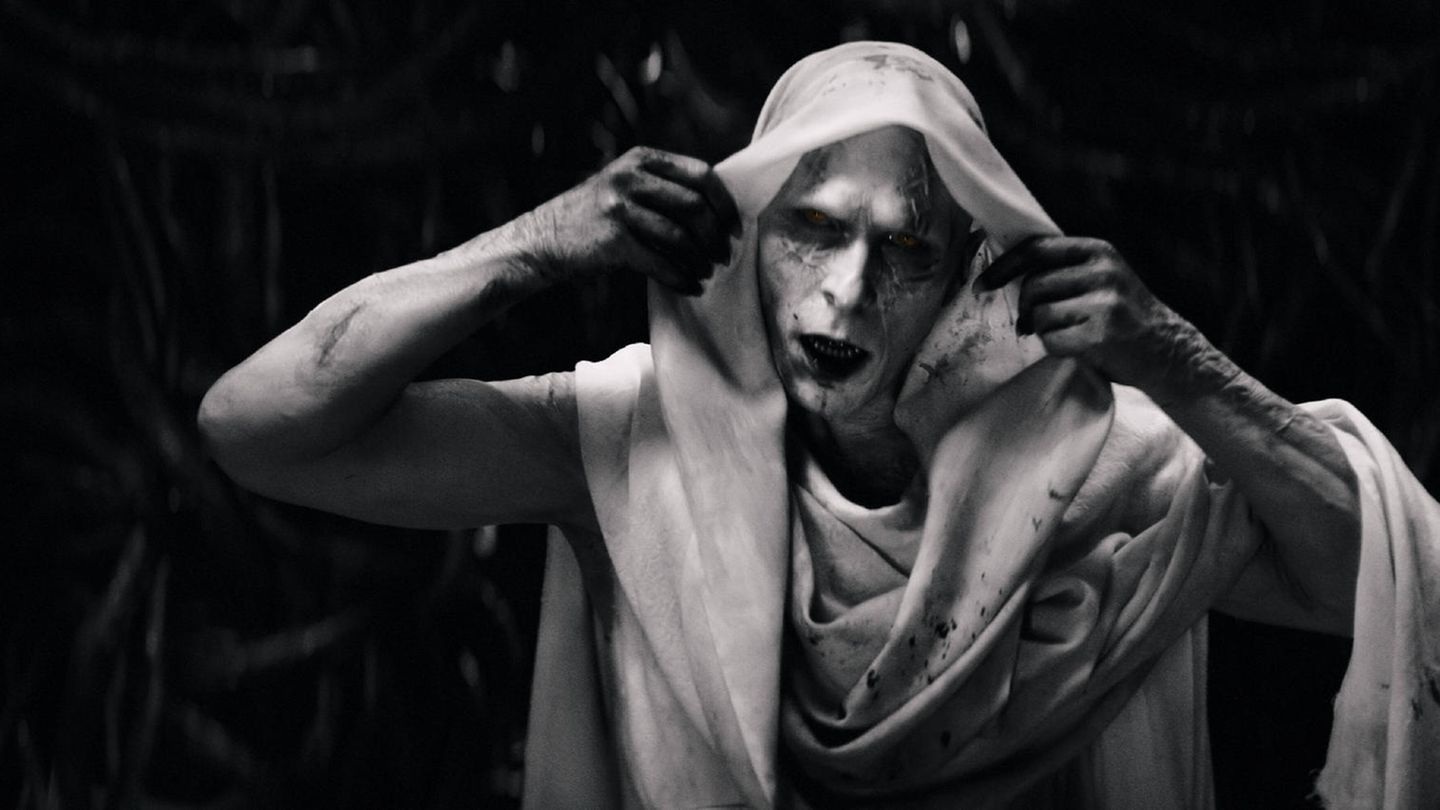 Christian Bale mit weißem Make-up und Tuch über dem Kopf