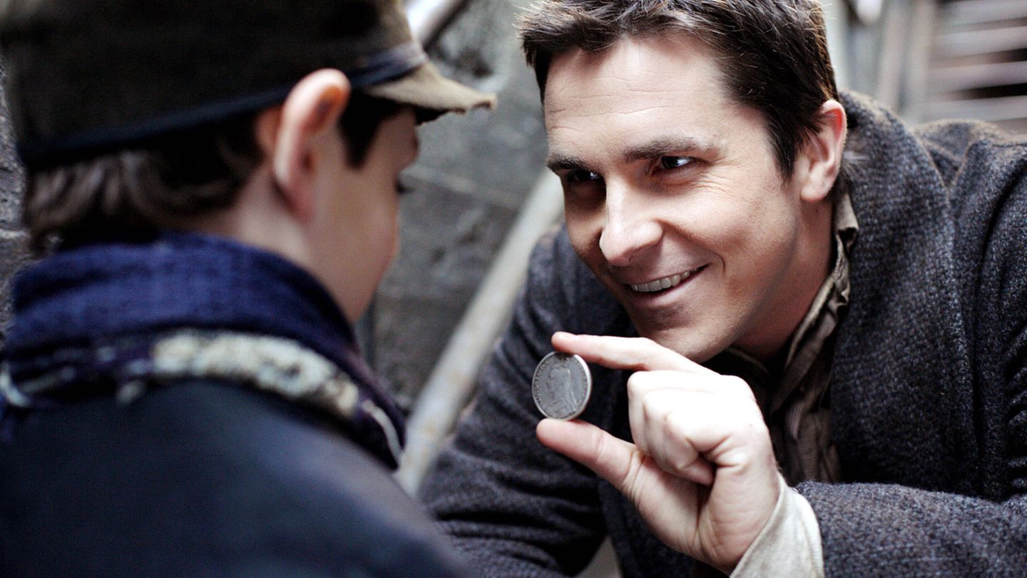 Christian Bale zeigt einem Jungen eine Münze