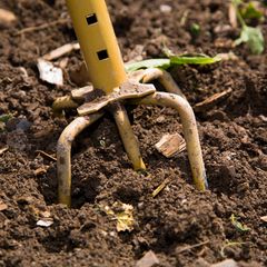 Eine Nahaufnahme eines Garten-"Klauen"-Werkzeugs, das in frisch bearbeitetem Boden gräbt