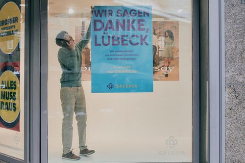 Ein Mitarbeiter der Karstadt-Filiale in Lübeck hängt ein Plakat von einer Scheibe ab