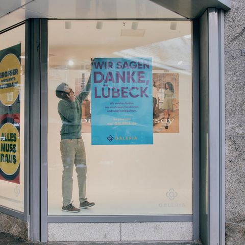 Ein Mitarbeiter der Karstadt-Filiale in Lübeck hängt ein Plakat von einer Scheibe ab
