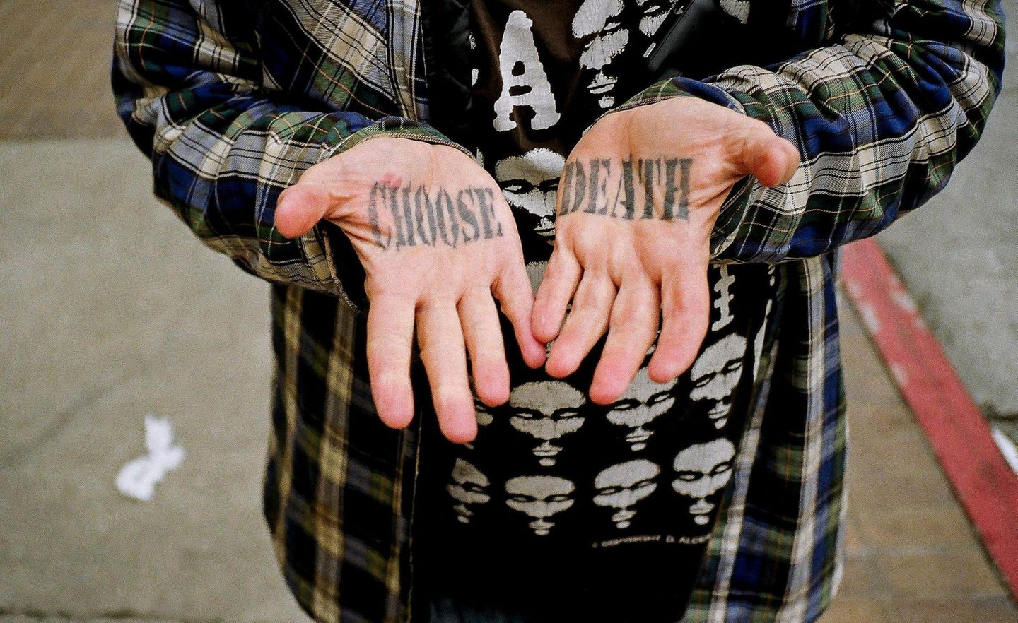 Ein Mann zeigt seine Hände, auf deren Innenflächen „Choose Death“ tätowiert ist