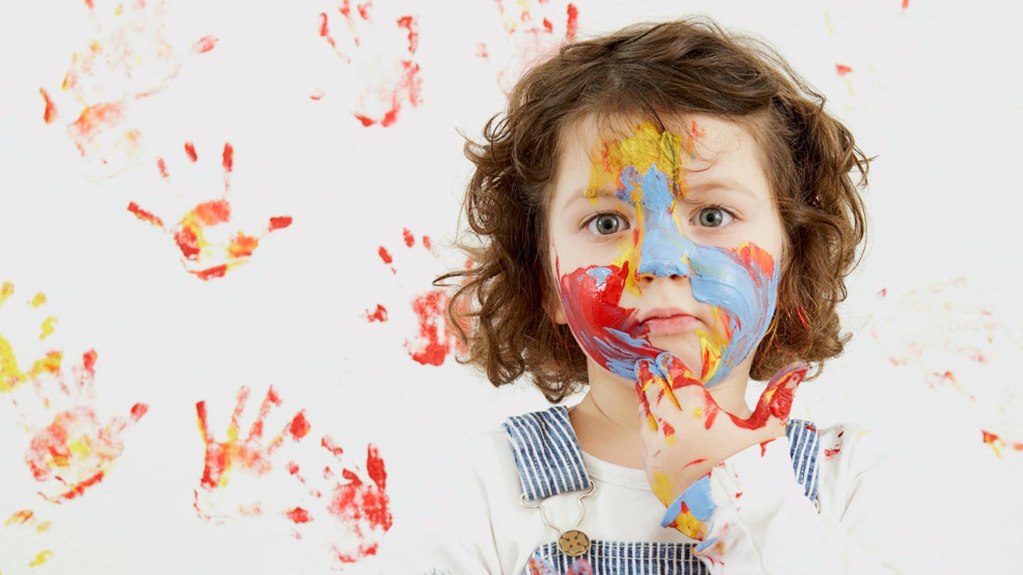 Eltern Ein Kind steht mit Farbverschmierten Händen vor einer Wand voller bunter Handabdrücke