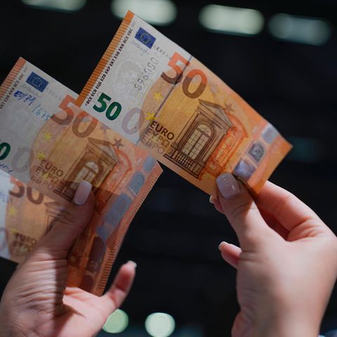 Eine Frau hält in der rechten Hand einen echten 50-Euro-Schein