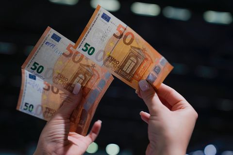 Eine Frau hält in der rechten Hand einen echten 50-Euro-Schein