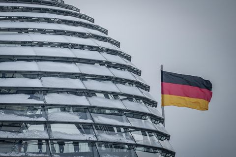 Die Deutschlandfahne weht neben der schneebedeckten Reichstagskuppel im Wind