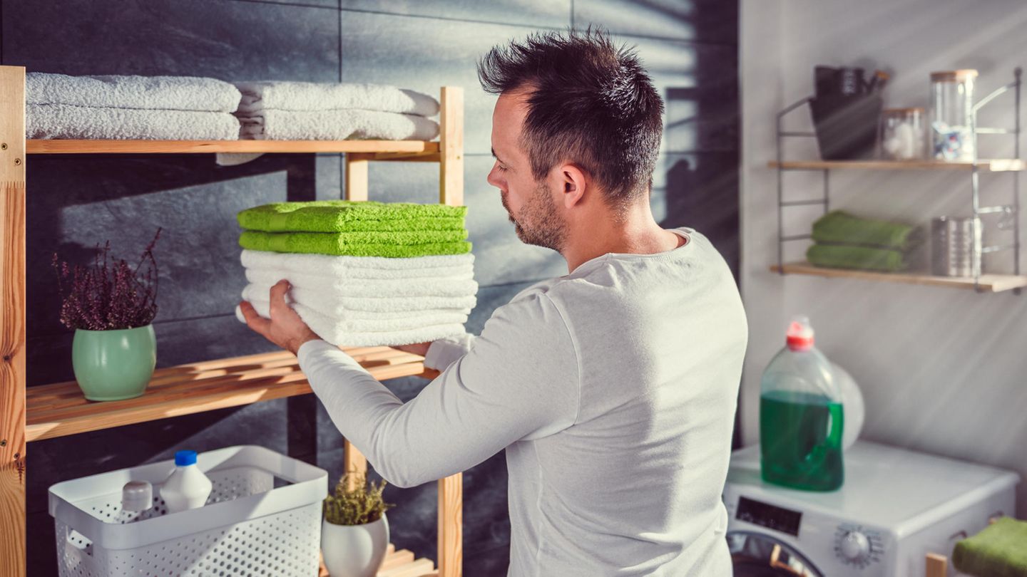 Waschküche einrichten: Mann legt Stapel Handtücher in Regal.
