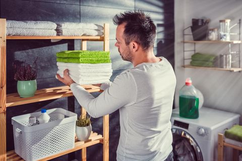 Waschküche einrichten: Mann legt Stapel Handtücher in Regal.