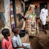 Drei Kinder betrachten einen Egungun in seinen Umhängen