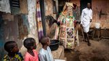 Drei Kinder betrachten einen Egungun in seinen Umhängen