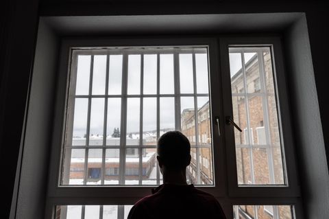 Die Silhouette eines Häftlings ist vor dem vergitterten Fenster einer JVA zu sehen