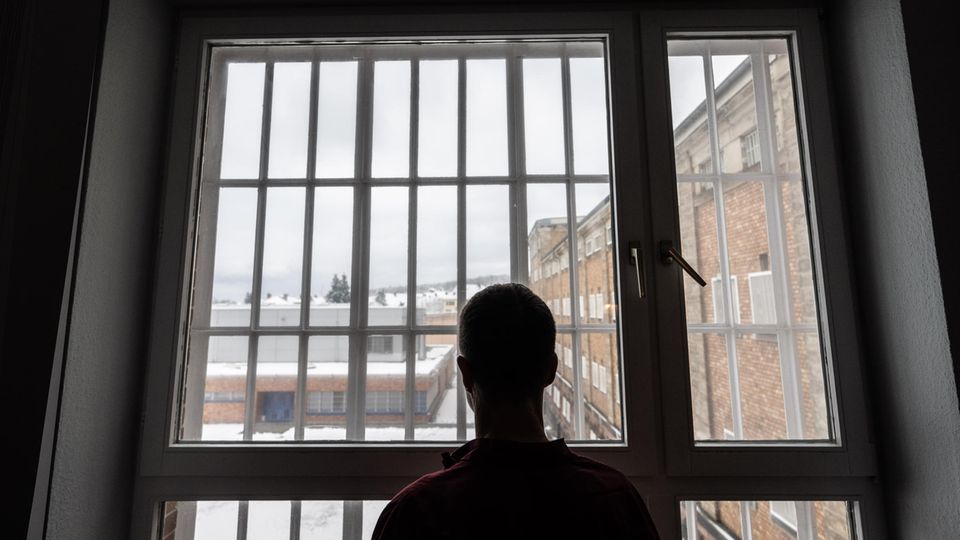 Die Silhouette eines Häftlings ist vor dem vergitterten Fenster einer JVA zu sehen