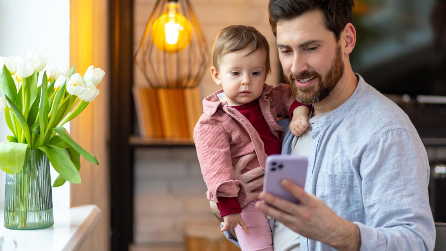 Geldanlage: Ein Mann mit einem Kind auf dem Arm und Smartphone in der Hand