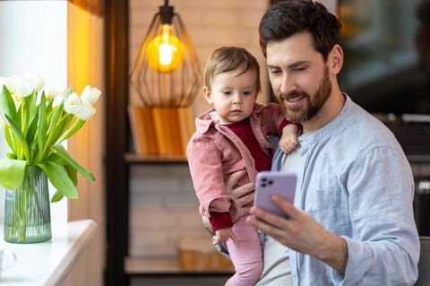 Geldanlage: Ein Mann mit einem Kind auf dem Arm und Smartphone in der Hand