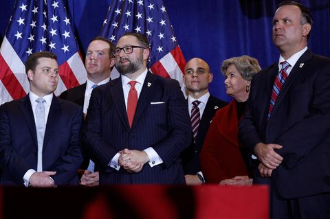 Fünf Männer in Anzügen und eine Frau im roten Blazer stehen auf einer Bühne: das Berater-Team von Donald Trump