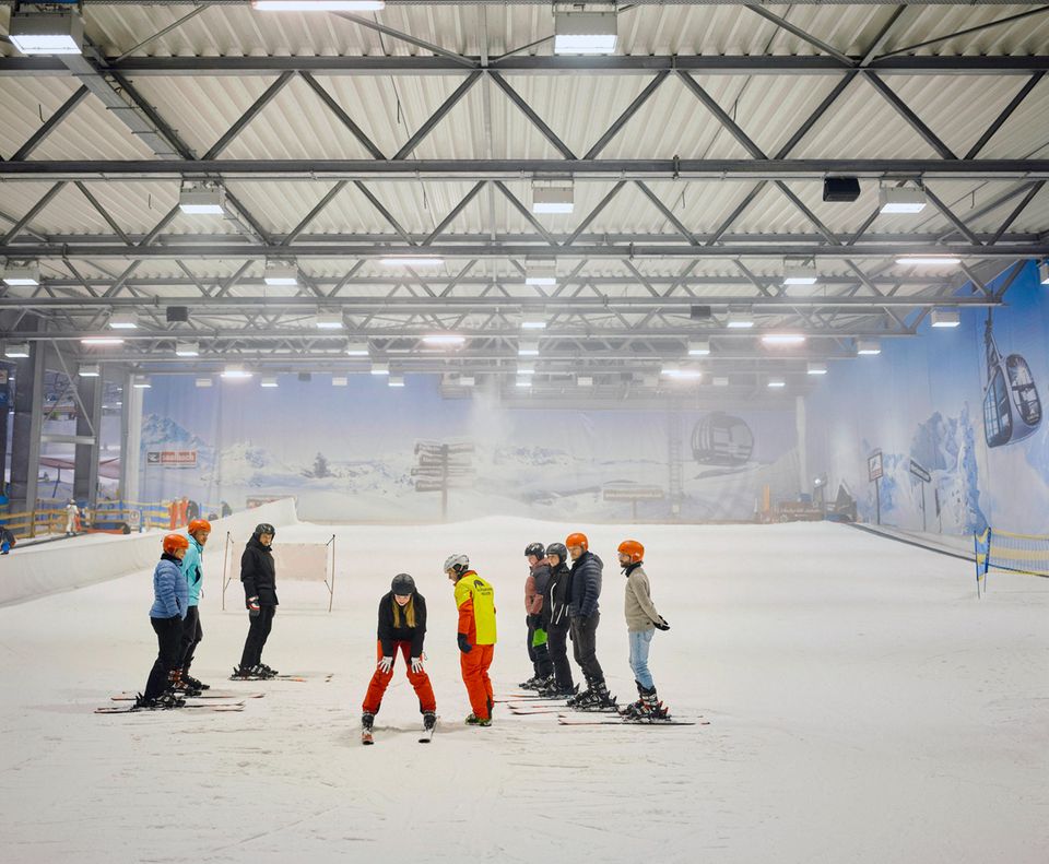 Menschen stehen auf Skiern in Schneeanzügen in der Skihalle Neuss