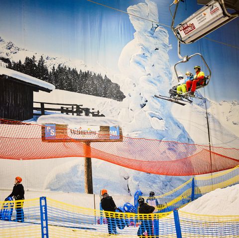 The gondola in the Neuss ski hall takes two skiers to the higher level, while other skiers stand below