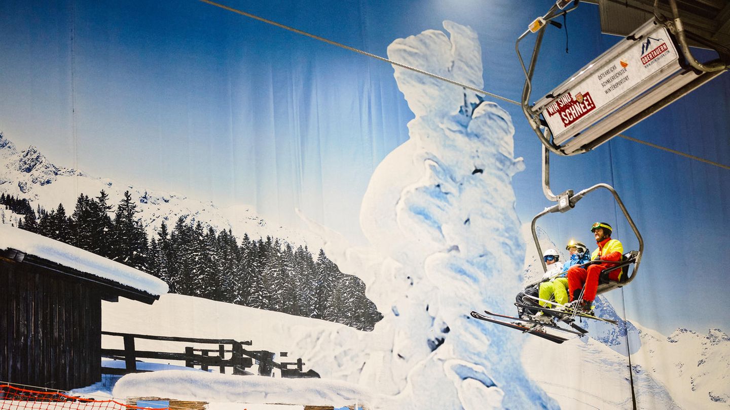 Gondel in der Skihalle Neuss bringt zwei Ski- Fahrer auf die höhere Ebene, unten stehen andere Ski-Fahrer