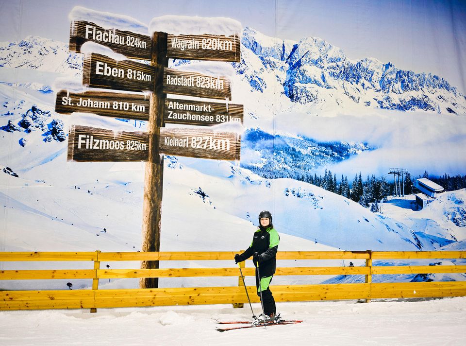 Skifahrerin steht von einer Fototapete in der Skihalle Neuss die eine Schneebedeckte Berglandschaft zeigt