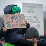 Ein kleines Mädchen hält ein Papp-Plakat in den Händen. Darauf heißt es: "Die Welt soll bunt sein und nicht braun."