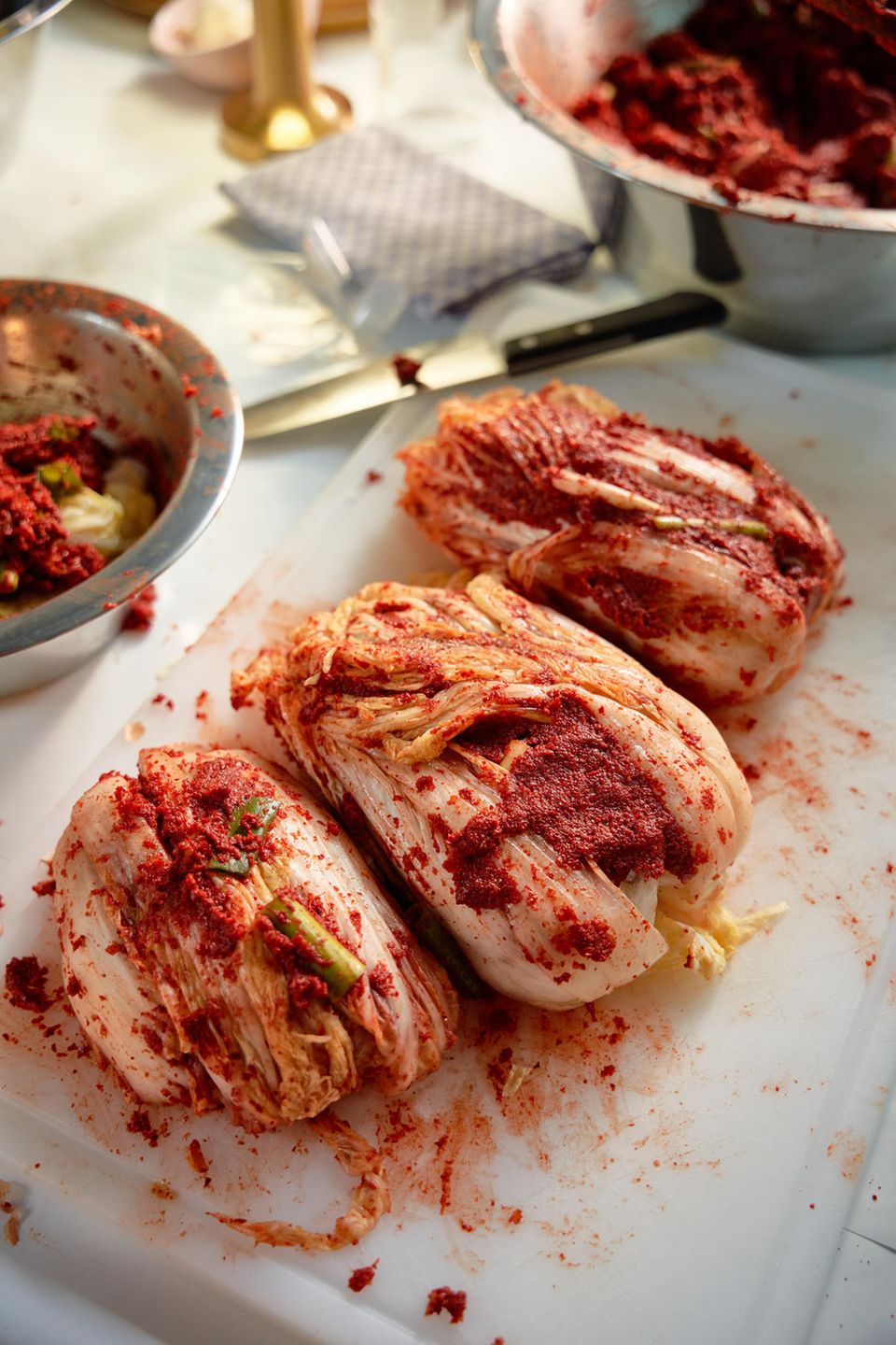 "Mr Susans" Kimchi-Rezept    Was Sie benötigen: 5 Kilo Napa-Kohl / Chinakohl (ca. 5 Köpfe Kohl), 300 g Salz  Für "Mr. Susans" Kimchi-Paste: 1 Knolle Knoblauch, 5 weiße/gelbe Zwiebeln, 3 Frühlingszwiebeln, ca. 1 Kilo, 150 Gramm Ingwer, eine halbe Ananas, etwa 600 g (aus der Dose ist OK, wenn keine Saison ist), , 200 Gramm koreanische Chiliflocken, (Optional) 1-2 Chilis Ihrer Wahl     Zubereitung:  1. Den Kohl vierteln (halbieren, dann wieder halbieren)  2. Schneiden Sie den Kohl in mundgerechte Stücke, ca. 3-4 cm  4. Kohlstücke großzügig salzen und vorsichtig durchschwenken. Darauf achten, dass das Salz gleichmäßig verteilt wird.  5. Den Kohl 2-3 Stunden im Salz liegen lassen. Der Kohl sollte weich werden und glänzen.  6. Die gesalzenen Kohlstücke vorsichtig waschen, jeweils eine Handvoll in ein Sieb geben. Den Kohl abtropfen lassen. 2-3 Stunden.  7. In der Zwischenzeit die Paste zubereiten. Dafür Knoblauch, Zwiebeln, Frühlingszwiebeln, Ingwer und Ananas grob hacken.  8. Alle Zutaten in einen Mixer geben und gründlich pürieren. Es sollte wie Apfelmus aussehen. Wasser oder etwas Ananassaft (100 ml) hinzufügen, wenn die Paste mehr Feuchtigkeit benötigt.  9. Nach dem Pürieren die koreanischen Chiliflocken hinzufügen und in die Paste einrühren. Die Paste sollte eine leuchtend rote Farbe haben. Die Konsistenz sollte fest, aber nicht trocken sein.  10. Die Paste gründlich unter den abgetropften Kohl mischen und gleichmäßig verteilen. YAY KIMCHI! Das Kimchi schmeckt frisch bereits sehr gut. ABER für noch mehr Geschmack - lassen Sie die Fermentation beginnen.  Tipp: Kimchi in einen luftdichten Behälter oder ein Glasgefäß füllen und vorsichtig nach unten drücken, damit die Luft herausgedrückt wird. Decken Sie das Kimchi oben mit Frischhaltefolie ab, damit keine Luft eindringt. Lassen Sie die Magie geschehen. Je länger es gärt, desto intensiver wird der Geschmack. Ich liebe es, wenn es etwa 3 Wochen alt ist, mein Vater hat Kimchi nur frisch gegessen, es durfte nicht älter als eine Woche sein. In Korea gibt es eine Delikatesse namens 'Mukkeunji' Kimchi, das über ein Jahr lang fermentiert wurde!  Machen Sie sich keine Sorgen wegen des "Champagner-Effekts", denn wenn Ihr Kimchi richtig gemacht wird, läuft Kimchi-Saft aus, was bedeutet, dass die Fermentierung funktioniert. #makeitsparkle