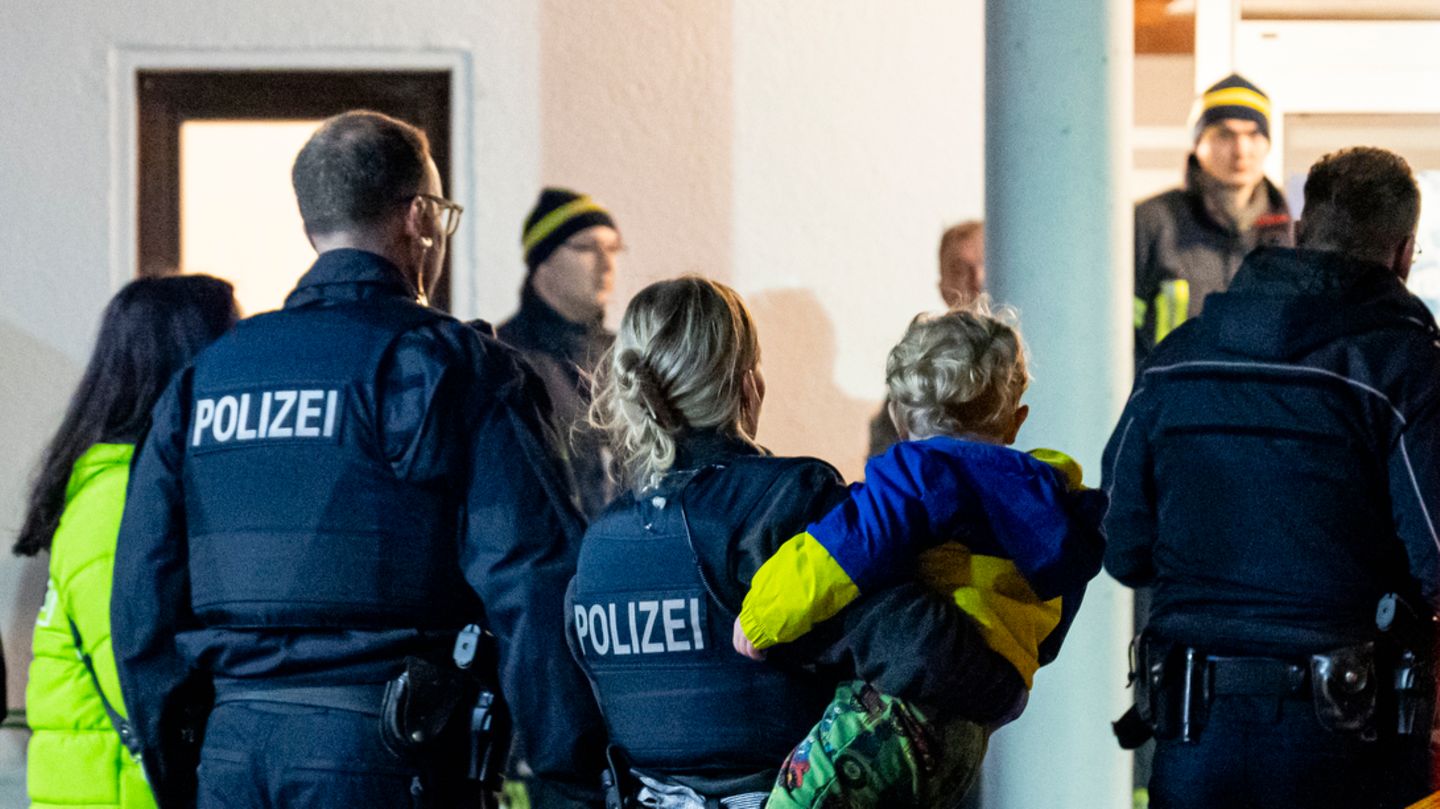 Ein blonder Zweijähriger sitzt im rechten Arm einer Polizistin in dunkelblauer Uniform