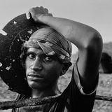 Ein Mann schaut in die Kamera, er hält ein schweres Stahlteil in den Händen