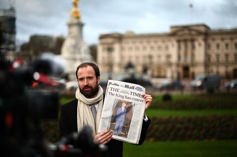 Das Schicksal des Königs hält die Nation in Atem: Ein Reporter berichtet die Lage vor dem Buckingham Palace in London. In seiner Hand hält er die Dienstagsausgabe der Times mit der Schlagzeile "Der König hat Krebs".