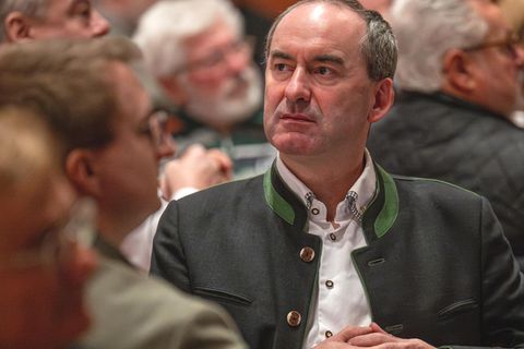 Hubert Aiwanger sitzt mit verschränkten Händen an einem Tisch bei einer Versammlung.