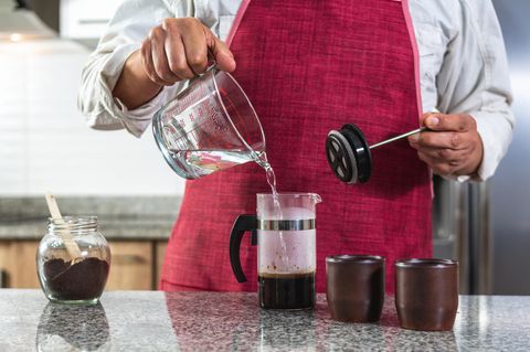 French Press Zubereitung: Mann mit Küchenschürze brüht einen Kaffee mit der French Press auf